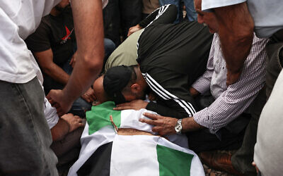 Une personne en deuil se penchant sur le corps drapé du drapeau de Hanan Abdel Rahman Abu Salama, 59 ans, qui aurait été tuée par des tirs israéliens alors qu'elle cueillait des olives dans le village cisjordanien de Faqoua, près de Jénine, lors de ses funérailles, le 17 octobre 2024. (Crédit : Zain Jaafar/AFP)