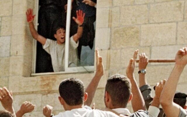 Le Palestinien Aziz Salha à une fenêtre, montrant ses mains tachées de sang, alors qu'une foule bat à mort deux soldats israéliens à Ramallah, en octobre 2000. (Crédit : Capture d'écran YouTube) Le Palestinien Aziz Salha à une fenêtre, montrant ses mains tachées de sang, alors qu'une foule bat à mort deux soldats israéliens à Ramallah, en octobre 2000. (Crédit : Capture d'écran YouTube)