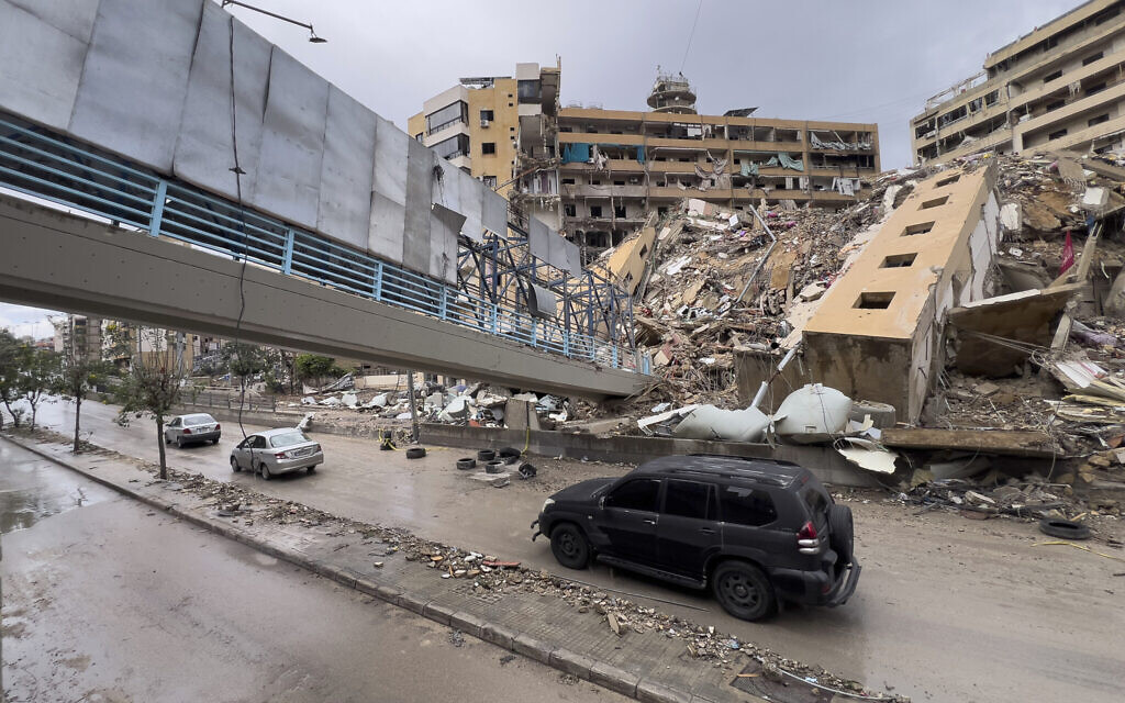 Des voitures passent sous un pont piétonnier effondré et à côté d'un bâtiment détruit par une frappe aérienne israélienne à Dahiyeh, dans la banlieue sud de Beyrouth, au Liban, le 19 novembre 2024. (Crédit : AP/Hussein Malla)