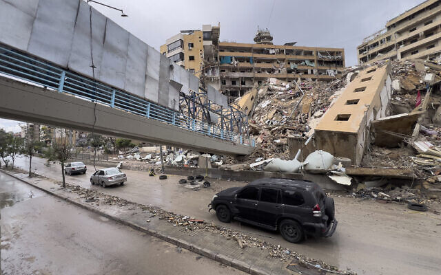 Des voitures passent sous un pont piétonnier effondré et à côté d'un bâtiment détruit par une frappe aérienne israélienne à Dahiyeh, dans la banlieue sud de Beyrouth, au Liban, le 19 novembre 2024. (Crédit : AP/Hussein Malla)
