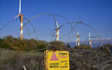 Des éoliennes d'énergie renouvelable vues à côté des pics enneigés du Mont Hermon le 3 janvier 2021, au nord du plateau du Golan, avec un panneau avertissant de la présence de mines terrestres. (Crédit : Michael Giladi/Flash90)