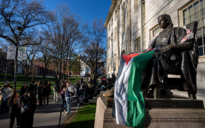 Des étudiants protestant contre la guerre à Gaza et des passants traversant Harvard Yard se tiennent près de la statue de John Harvard, le premier grand bienfaiteur de Harvard College, drapée dans le drapeau palestinien, dans le campement de l'Université de Harvard à Cambridge, Massachusetts, le 25 avril 2024. Illustration (Crédit : Ben Curtis/AP)