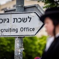 Un homme ultra-orthodoxe, devant un panneau indiquant un bureau de recrutement de l’armée israélienne lors d'une manifestation contre la conscription des hommes haredim dans l'armée, à Jérusalem, le 1er mai 2024. (Crédit : Yonatan Sindel/Flash90)