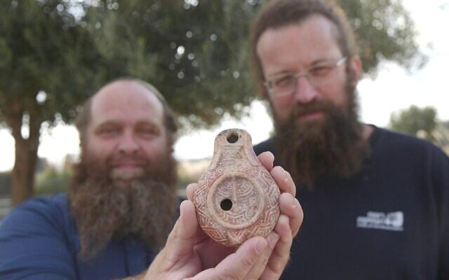 Michael Chernin (G) et Benjamin Storchan tenant une lampe à huile vieille de 1 700 ans, décorée de la ménorah du Temple, découverte à Jérusalem. Photo publiée le 26 décembre 2024. (Crédit : Emil Aladjem/Autorité israélienne des Antiquités)