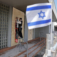 Un membre de la communauté juive agrafe une affiche sur la façade de la synagogue Adass Israel endommagée à Ripponlea, dans la banlieue de Melbourne, le 9 décembre 2024. (Crédit : Martin KEEP / AFP)