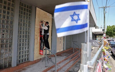 Un membre de la communauté juive agrafe une affiche sur la façade de la synagogue Adass Israel endommagée à Ripponlea, dans la banlieue de Melbourne, le 9 décembre 2024. (Crédit : Martin KEEP / AFP)