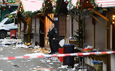 Des débris et des stands fermés  visibles alors qu'un officier de police se tient sur le site d'un attentat à la voiture-bélier sur un marché de Noël, à Magdebourg, dans l'est de l'Allemagne, le 21 décembre 2024, qui a fait plusieurs morts et des dizaines de blessés. Les médias allemands rapportent que le nombre de morts est passé à quatre dans la nuit et qu'il y a eu jusqu'à 200 blessés dans l'attentat du 20 décembre 2024. (Crédit : John Macdougall/AFP)