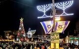 Des gens marchant sur un marché de Noël près d'un arbre de Noël illuminé, d'une lanterne de Ramadan et d'une menorah de Hanoukka, dans le quartier de la colonie allemande à Haïfa, le 21 décembre 2024. (Crédit : Ahmad Gharabli/AFP)