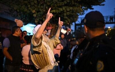 Un membre de la secte juive Lev Tahor proteste alors que des membres de la police guatémaltèque entourent un minibus transportant des enfants sauvés vers l'école d'éducation spécialisée Alida Espana de Arana à Guatemala City le 22 décembre 2024. (Crédit : Johan ORDÓÑEZ / AFP)