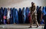 Un combattant taliban montant la garde alors que des femmes attendent de recevoir des rations alimentaires distribuées par un groupe d'aide humanitaire, à Kaboul, en Afghanistan, le 23 mai 2023. (Crédit : Ebrahim Noroozi/AP)