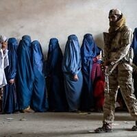 Un combattant taliban montant la garde alors que des femmes attendent de recevoir des rations alimentaires distribuées par un groupe d'aide humanitaire, à Kaboul, en Afghanistan, le 23 mai 2023. (Crédit : Ebrahim Noroozi/AP)