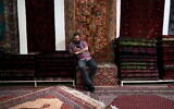 Un vendeur sur son téléphone portable, dans un magasin de tapis, dans le vieux bazar principal de Téhéran, en Iran, le 13 juin 2024. (Crédit : Vahid Salemi/AP)
