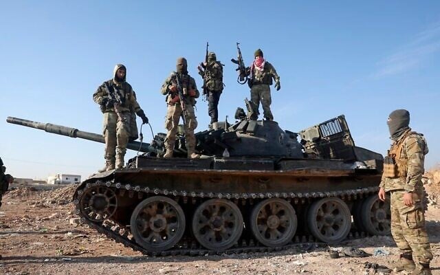Des insurgés islamistes syriens se tiennent sur un véhicule blindé de l'armée syrienne saisi dans la banlieue de Hama, en Syrie, le mardi 3 décembre 2024. (Crédit : AP Photo/Ghaith Alsayed)