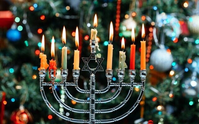 Une hanoukkiya allumée, et un sapin de Noël en arrière-plan. (Crédit : Photovs/iStock)
