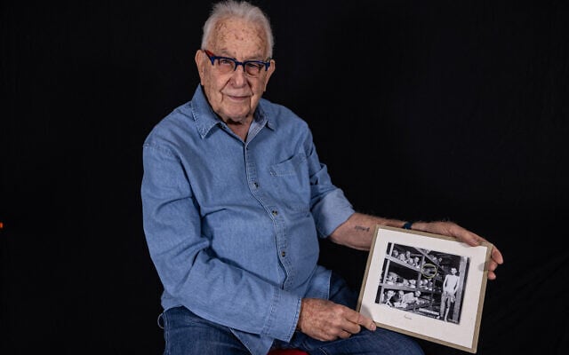 Naftali Furst, survivant de la Shoah, tient une photo de lui prise en 1945 dans l'une des baraques du camp de concentration de Buchenwald, alors qu'il pose dans sa maison de la ville de Haïfa, dans le nord d'Israël, le 28 novembre 2024. (Crédit : Menahem Kahana / AFP)