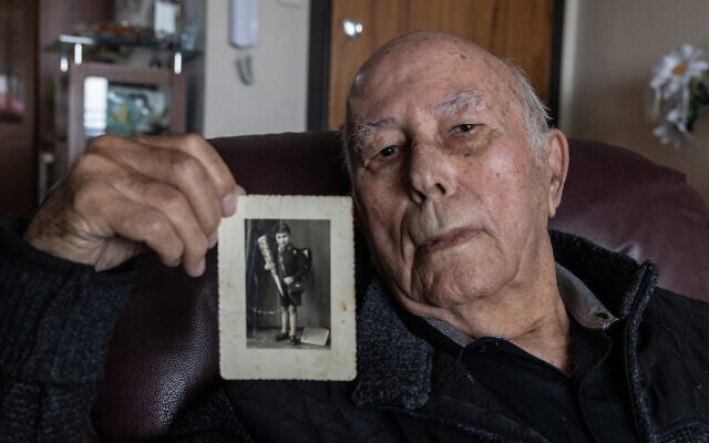 Avraham Wassertheil, survivant de la Shoah, tient une photo de lui enfant en Allemagne, dans sa maison de la ville de Kiryat Yam, dans le nord d'Israël, le 12 décembre 2024. (Crédit : MENAHEM KAHANA / AFP)