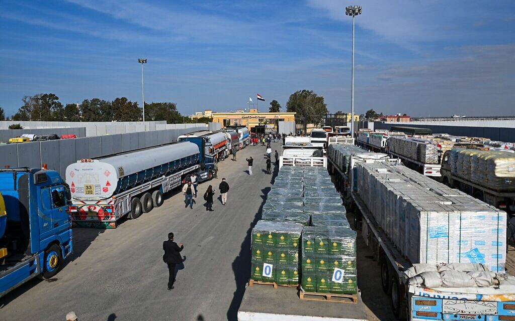 Des personnes passent devant des camions chargés d'aide qui attendent de passer à Gaza du côté égyptien du poste frontière de Rafah, le 19 janvier 2025. (Crédit : Khaled Desouki/AFP) Des personnes passent devant des camions chargés d'aide qui attendent de passer à Gaza du côté égyptien du poste frontière de Rafah, le 19 janvier 2025. (Crédit : Khaled Desouki/AFP)