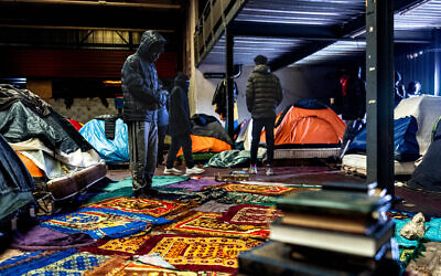 Un migrant (à gauche) prie à l'intérieur d'un entrepôt à Marck, près de Calais, dans le nord de la France, le 24 janvier 2025. Dans la zone industrielle de Calais, des centaines de migrants vivent dans un hangar, protégés de la pluie mais exposés au froid, au vent et à l'humidité. Face à une réponse d'urgence des autorités jugée insuffisante, Médecins sans frontières (MSF) héberge les migrants dans un hôtel depuis le début de l'hiver. (Photo Sameer Al-DOUMY / AFP)