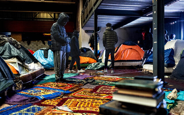 Un migrant (à gauche) prie à l'intérieur d'un entrepôt à Marck, près de Calais, dans le nord de la France, le 24 janvier 2025. Dans la zone industrielle de Calais, des centaines de migrants vivent dans un hangar, protégés de la pluie mais exposés au froid, au vent et à l'humidité. Face à une réponse d'urgence des autorités jugée insuffisante, Médecins sans frontières (MSF) héberge les migrants dans un hôtel depuis le début de l'hiver. (Photo Sameer Al-DOUMY / AFP) Un migrant (à gauche) prie à l'intérieur d'un entrepôt à Marck, près de Calais, dans le nord de la France, le 24 janvier 2025. Dans la zone industrielle de Calais, des centaines de migrants vivent dans un hangar, protégés de la pluie mais exposés au froid, au vent et à l'humidité. Face à une réponse d'urgence des autorités jugée insuffisante, Médecins sans frontières (MSF) héberge les migrants dans un hôtel depuis le début de l'hiver. (Photo Sameer Al-DOUMY / AFP)