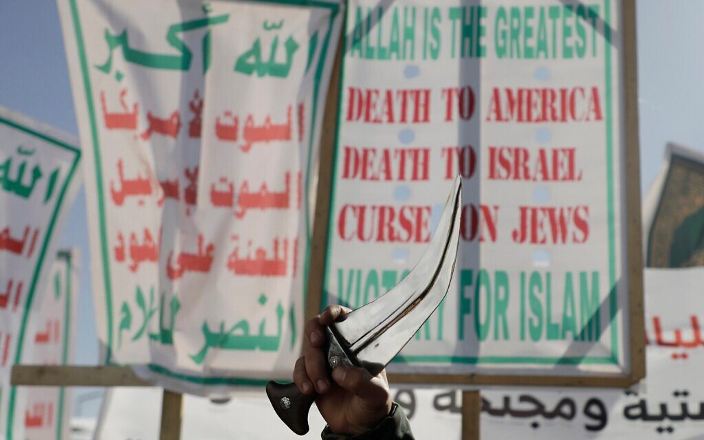 Un militant houthi brandit sa dague lors d'un rassemblement contre les États-Unis et Israël à Sanaa, au Yémen, le 17 janvier 2025, tandis que d'autres partisans du groupe rebelle soutenu par l'Iran brandissent des banderoles avec son slogan. (AP Photo/Osamah Abdulrahman)