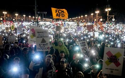 Des personnes brandissant leur téléphone portable protestent contre le parti d'extrême droite Alternative pour l'Allemagne (AfD) et l'extrémisme de droite, devant la porte de Brandebourg, à Berlin, en Allemagne, le 25 janvier 2025. (Crédit : Ebrahim Noroozi/AP)