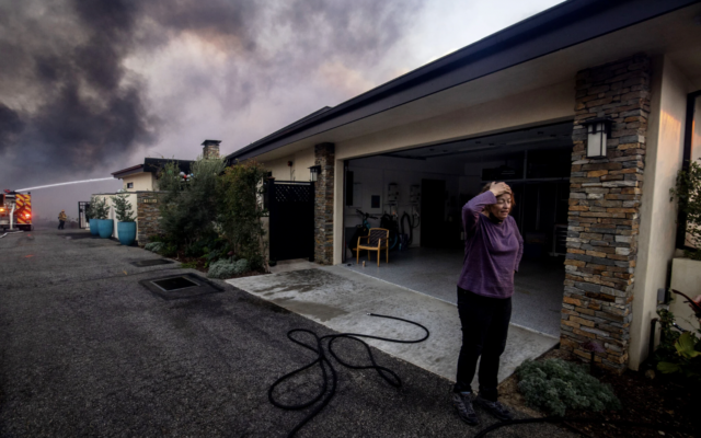 Une habitante devant son garage alors que les équipes de pompiers combattent l'incendie de Palisades à proximité, dans le quartier de Pacific Palisades, à Los Angeles, le 7 janvier 2025. (Crédit : Ethan Swope/AP)