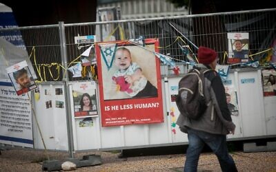 Une personne passant devant des photographies d'Israéliens pris en otage par des terroristes du Hamas à Gaza, dont le bébé Kfir Bibas, sur la Place des Otages, à Tel Aviv, le 14 février 2024. (Crédit : Miriam Alster/Flash90)