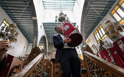 Henry Hamra tient un rouleau de Torah alors qu'il visite la synagogue al-Franj dans le quartier juif de Damas, le 18 février 2025. (Crédit : Louai Beshara/AFP)