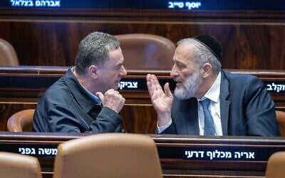 Le ministre de la Défense Israel Katz (à gauche) s'adresse au chef du Shas Aryeh Deri lors d'un vote à la Knesset le 31 décembre 2024. (Chaim Goldberg/Flash90)