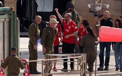 L'ex-otage israélo-argentin Yaïr Horn (au centre en rouge), portant un maillot de football du Hapoel Beer Sheva, entouré de ses proches et des forces de sécurité, faisant un geste après être descendu d'un hélicoptère militaire sur l'héliport du centre hospitalier Sourasky de Tel Aviv, le 15 février 2025. (Crédit : Jack Guez/AFP)