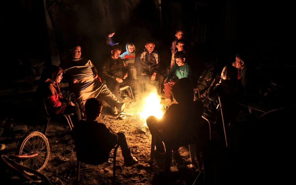 Des Palestiniens s'assoient autour d'un feu en extérieur, au milieu des ruines de leurs maisons à Jabalia dans le nord de la bande de Gaza, le 18 février 2025 (Omar AL-QATTAA / AFP)