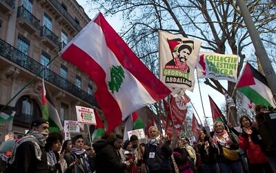 Un manifestant brandit le drapeau libanais et un drapeau sur lequel est écrit en français « Libérez Georges Abdallah » lors d'un rassemblement à Toulouse pour exiger la libération de l'assassin pro-palestinien libanais Georges Ibrahim Abdallah, le 19 février 2025. (Crédit : Matthieu RONDEL / AFP)