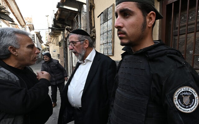 Un garde de sécurité local, affilié à la nouvelle administration en Syrie, se tient à côté du rabbin syrien basé aux États-Unis, Youssef Hamra, alors qu'il parle aux gens à l'extérieur de la synagogue Ifrange dans le quartier juif du district de Bab Sharqi à Damas, le 19 février 2025. (Crédit : LOUAI BESHARA / AFP)