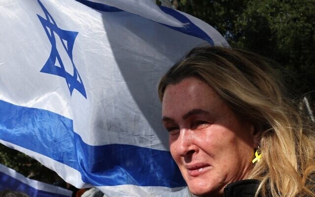 Une Israélienne pleurant en agitant le drapeau national à l'arrivée du convoi de véhicules transportant ce que l'on pense être les corps de quatre otages israéliens remis par le Hamas, à l'Institut médico-légal, à Tel Aviv, le 20 février 2025. (Crédit : Jack Guez/AFP)