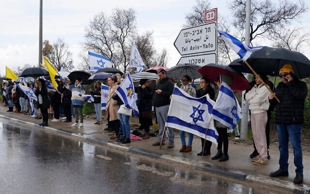 Des personnes rendant hommage en attendant un convoi transportant les corps de quatre otages israéliens près de la ville de Sderot, dans le sud du pays, le 20 février 2025. (Crédit : John Wessels/AFP)