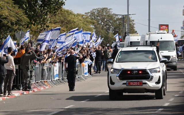 Des Israéliens brandissant le drapeau national à l'arrivée du convoi de véhicules transportant les corps des quatre otages israéliens remis par le Hamas à l'entrée de l'Institut médico-légal, à Tel Aviv, le 20 février 2025. (Crédit : Jack Guez/AFP)
