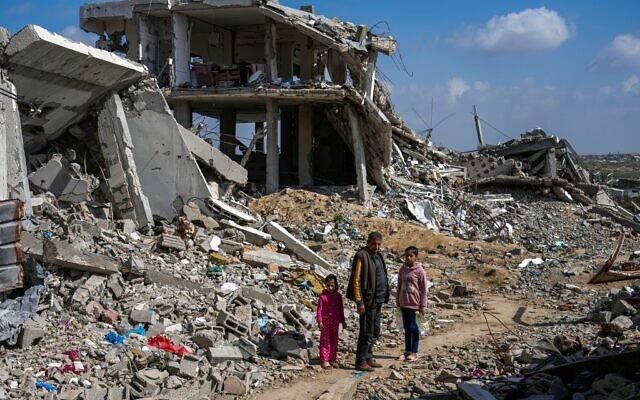 Un Palestinien et deux fillettes au milieu des décombres de maisons détruites pendant la guerre entre Israël et le Hamas dans le camp de réfugiés de Bureij, dans le centre de la bande de Gaza, le 17 février 2025. (Crédit : Abdel Kareem Hana/AP)