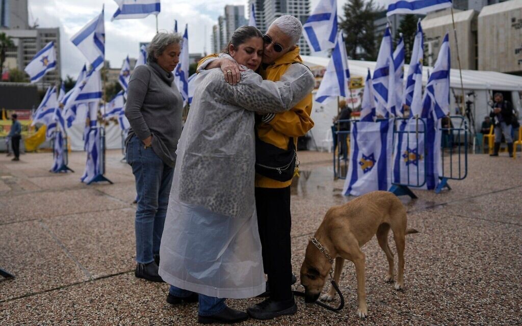 Deux personnes s'étreignant avant la remise par le Hamas des corps de quatre otages israéliens dans la bande de Gaza, sur la Place des Otages, à Tel Aviv, le 20 février 2025. (Crédit : Oded Balilty/AP)