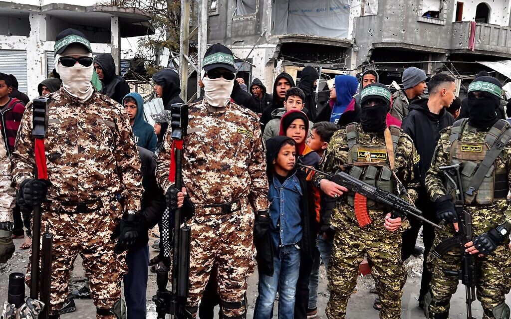 Des terroristes armés des Brigades Ezzedine al-Qassam montant la garde pendant que des Palestiniens attendent la remise des otages israéliens à la Croix-Rouge, à Rafah, le 22 février 2025. (Crédit : Saeed Mohammed/Flash90)