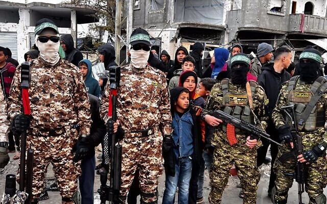 Des terroristes armés des Brigades Ezzedine al-Qassam montant la garde pendant que des Palestiniens attendent la remise des otages israéliens à la Croix-Rouge, à Rafah, le 22 février 2025. (Crédit : Saeed Mohammed/Flash90)
