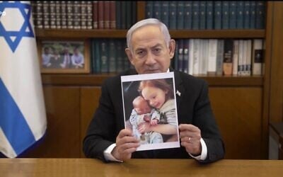 Le Premier ministre Benjamin Netanyahu tenant une photo d'Ariel et de Kfir Bibas, dans un message vidéo, le 21 février 2025. (Crédit : Capture d'écran/GPO)