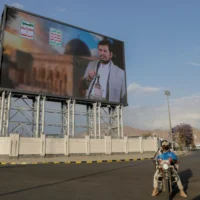 Des Yéménites passent sous un panneau d'affichage affichant une photo d'Abdul Malik al-Houthi, le chef du groupe rebelle Houthi. Le texte en arabe dit « mort à l'Amérique, mort à Israël », à Sanaa, Yémen, mardi 18 mars 2025. (Crédit : Osamah Abdulrahman/AP)