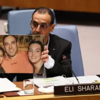 L’ex-otage Eli Sharabi montre une photo de sa famille - dont la femme, Lianne, et leurs filles, Noiya, 16 ans, et Yahel, 13 ans, ont été assassinées par des terroristes dans la pièce sécurisée de leur maison au kibboutz Beeri le 7 octobre 2023 ; Sharabi et son frère aîné Yossi ont été kidnappés, la mort de ce dernier a été confirmée et le Hamas détient sa dépouille - lors de son adresse au Conseil de sécurité des Nations Unies, à New York le 20 mars 2025. (Crédit : Michael M. Santiago/Getty Images/AFP)