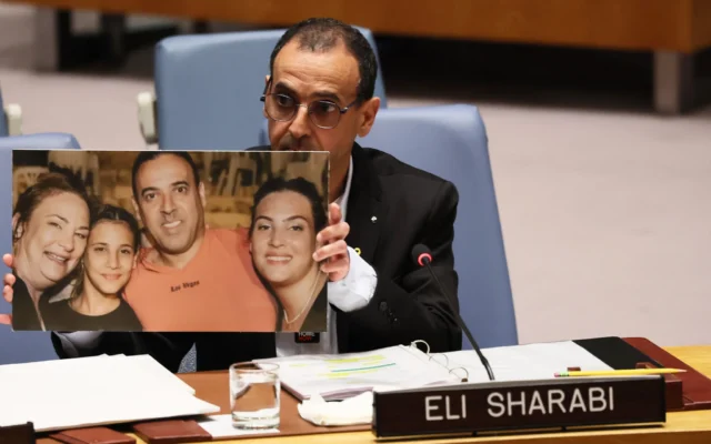 L’ex-otage Eli Sharabi montre une photo de sa famille - dont la femme, Lianne, et leurs filles, Noiya, 16 ans, et Yahel, 13 ans, ont été assassinées par des terroristes dans la pièce sécurisée de leur maison au kibboutz Beeri le 7 octobre 2023 ; Sharabi et son frère aîné Yossi ont été kidnappés, la mort de ce dernier a été confirmée et le Hamas détient sa dépouille - lors de son adresse au Conseil de sécurité des Nations Unies, à New York le 20 mars 2025. (Crédit : Michael M. Santiago/Getty Images/AFP) L’ex-otage Eli Sharabi montre une photo de sa famille - dont la femme, Lianne, et leurs filles, Noiya, 16 ans, et Yahel, 13 ans, ont été assassinées par des terroristes dans la pièce sécurisée de leur maison au kibboutz Beeri le 7 octobre 2023 ; Sharabi et son frère aîné Yossi ont été kidnappés, la mort de ce dernier a été confirmée et le Hamas détient sa dépouille - lors de son adresse au Conseil de sécurité des Nations Unies, à New York le 20 mars 2025. (Crédit : Michael M. Santiago/Getty Images/AFP)