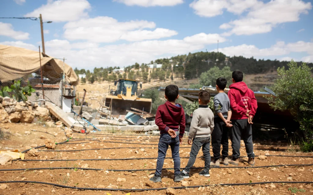 Des enfants palestiniens regardent l'administration civile israélienne démolir une maison à At-Tuwani, un village de Masafer Yatta, le 7 mai 2025. (Crédit : Emily Glick) Des enfants palestiniens regardent l'administration civile israélienne démolir une maison à At-Tuwani, un village de Masafer Yatta, le 7 mai 2025. (Crédit : Emily Glick)