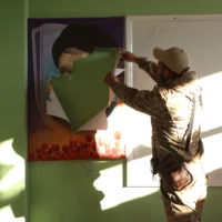 Un combattant rebelle syrien déchire un portrait du chef du Hezbollah assassiné, Hassan Nasrallah, dans un bâtiment qui aurait été utilisé par le groupe terroriste libanais Hezbollah, dans la ville de Qoussair, dans la province de Homs, au centre de la Syrie, le 15 décembre 2024. (Crédit : AAREF WATAD / AFP)