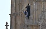 Un manifestant muni d'un drapeau palestinien et d'un keffieh, le poing levé, depuis le côté de la tour Elizabeth, communément appelée « Big Ben » en référence à la cloche de l'horloge, au palais de Westminster, siège des Chambres du Parlement, dans le centre-ville de Londres, le 8 mars 2025. (Crédit : Ben Stansall/AFP)