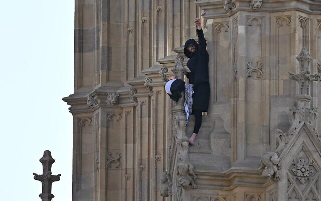 Un manifestant muni d'un drapeau palestinien et d'un keffieh, le poing levé, depuis le côté de la tour Elizabeth, communément appelée « Big Ben » en référence à la cloche de l'horloge, au palais de Westminster, siège des Chambres du Parlement, dans le centre-ville de Londres, le 8 mars 2025. (Crédit : Ben Stansall/AFP)
