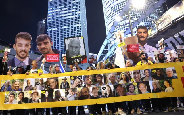 Des amis et des proches d'otages israéliens retenus captifs par des terroristes à Gaza se tiennent derrière une banderole portant leurs portraits lors d'une manifestation réclamant leur libération, devant le ministère de la Défense à Tel Aviv, le 11 mars 2025. (Crédit : Jack Guez/AFP)