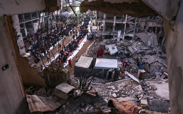 Les Palestiniens rassemblés pour un repas d'Iftar de rupture du jeûne au milieu des décombres de bâtiments détruits à Beit Lahiya, dans le nord de la bande de Gaza, le 15 mars 2025. (Crédit : Omar AL-Qattaa/AFP)
